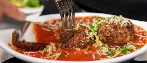 Une assiette de boulettes de viande nappées de sauce tomate, saupoudrées de fromage râpé et d’herbes aromatiques.