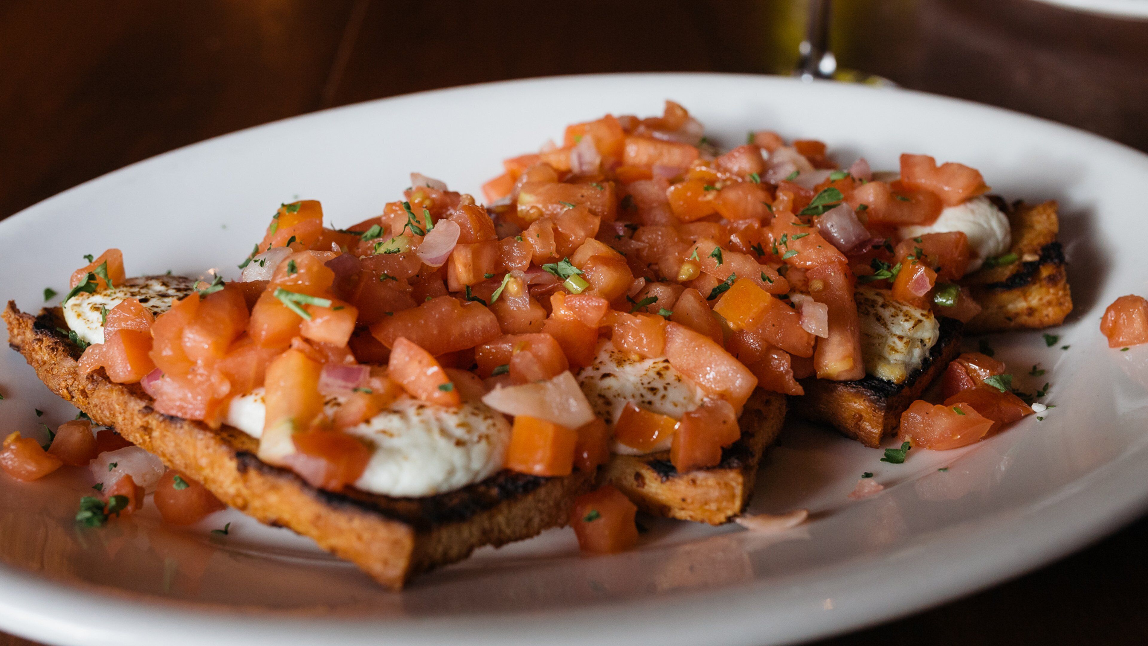 Una fuente de bruschetta coronada con tomates, cebollas y hierbas picadas.