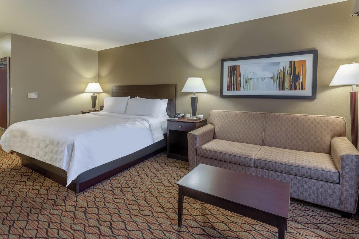 A hotel room with a bed, a sofa, a coffee table, two bedside tables with lamps, and a framed picture on the wall.