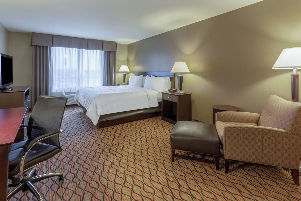 A hotel room with a bed, two bedside tables with lamps, a desk with a chair, and a sofa.