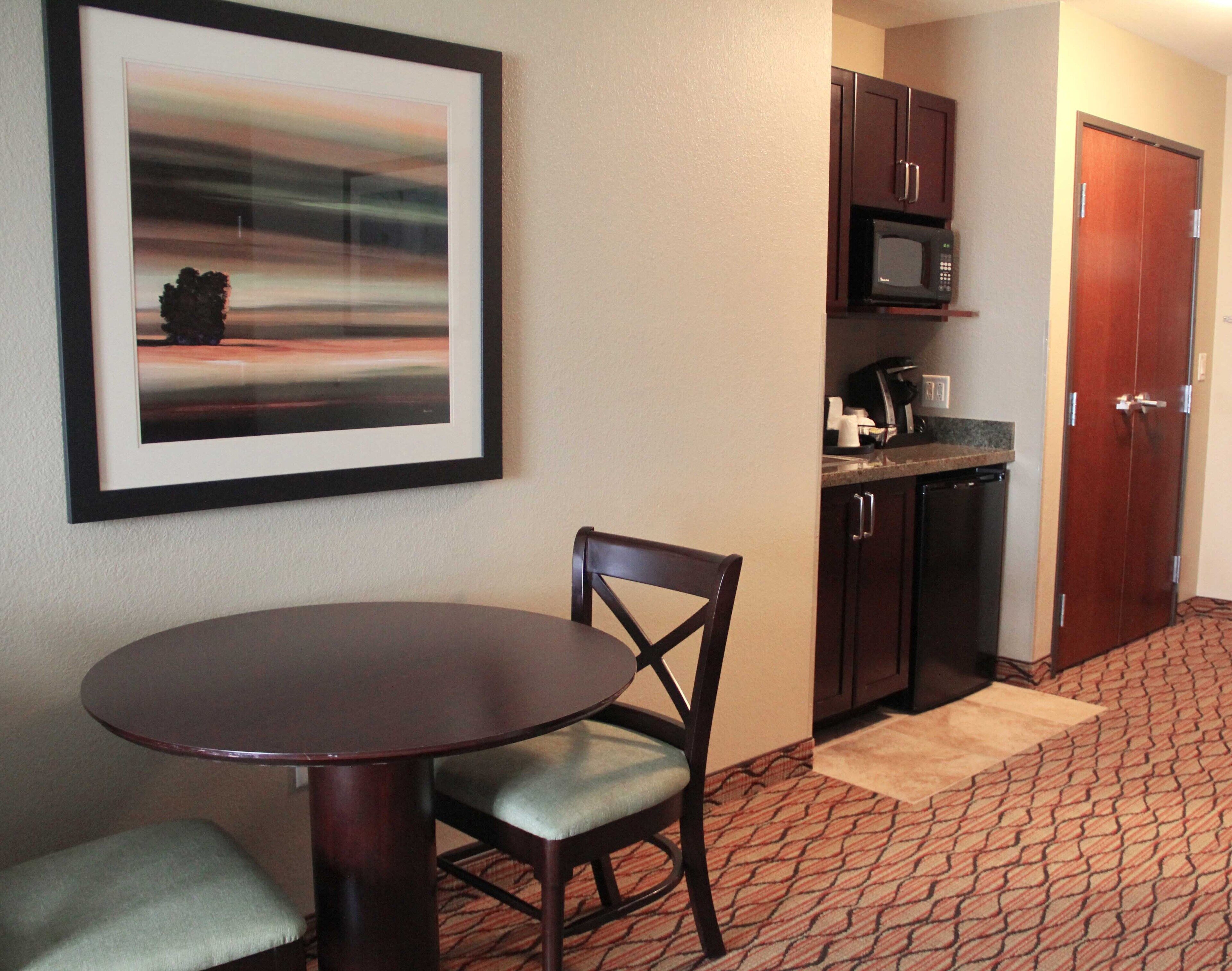 A small dining area with a round table and a chair, a microwave, and a cabinet in a hotel room.