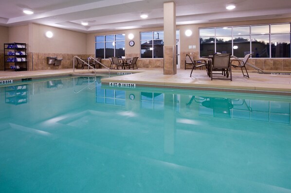 Une piscine intérieure dotée de chaises longues et offrant une vue sur l’extérieur.