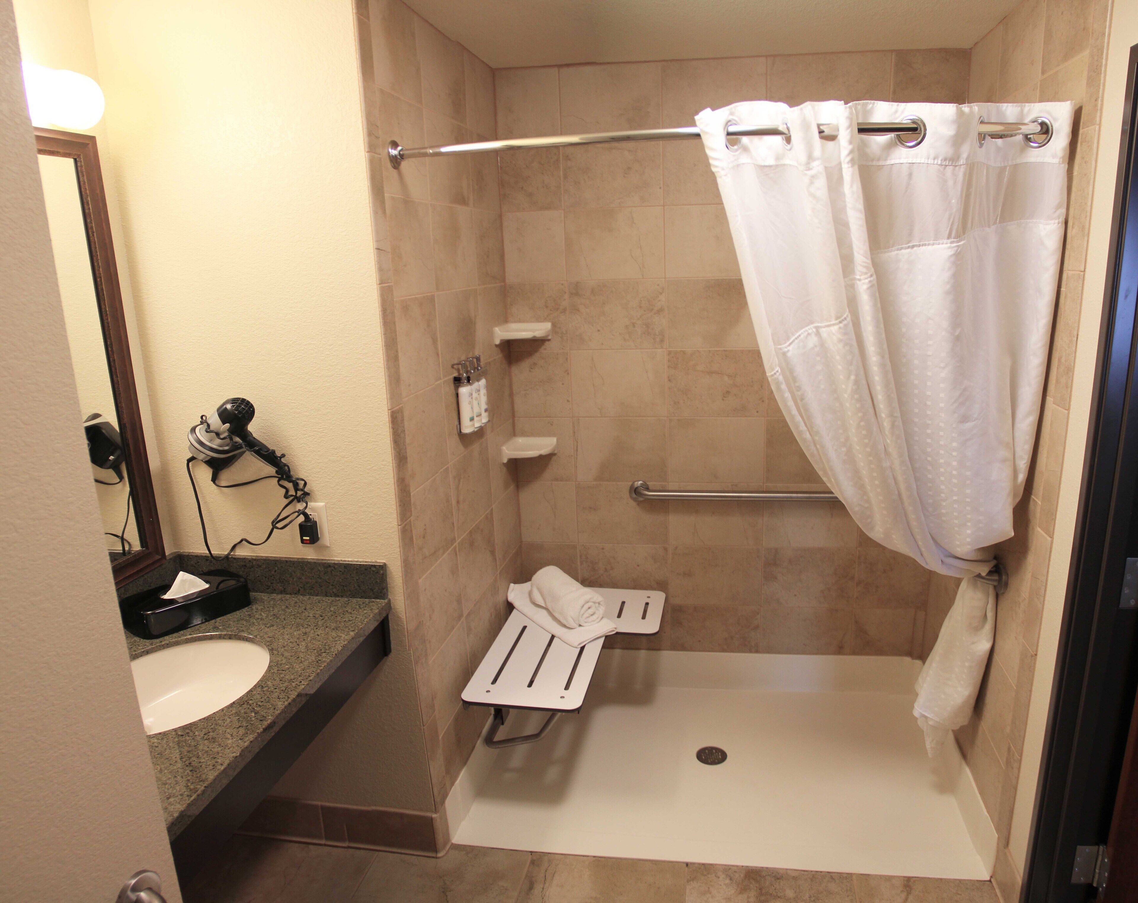 A small, walk-in shower with a white shower curtain, a towel rack, and a hand dryer.