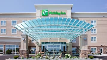 Un hotel Holiday Inn con un moderno toldo de cristal, fachada de piedra y un área de entrada ajardinada.