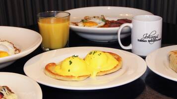 A breakfast setting with various dishes including eggs Benedict, a glass of orange juice, and a mug labeled "Johnny's Italian Steakhouse".