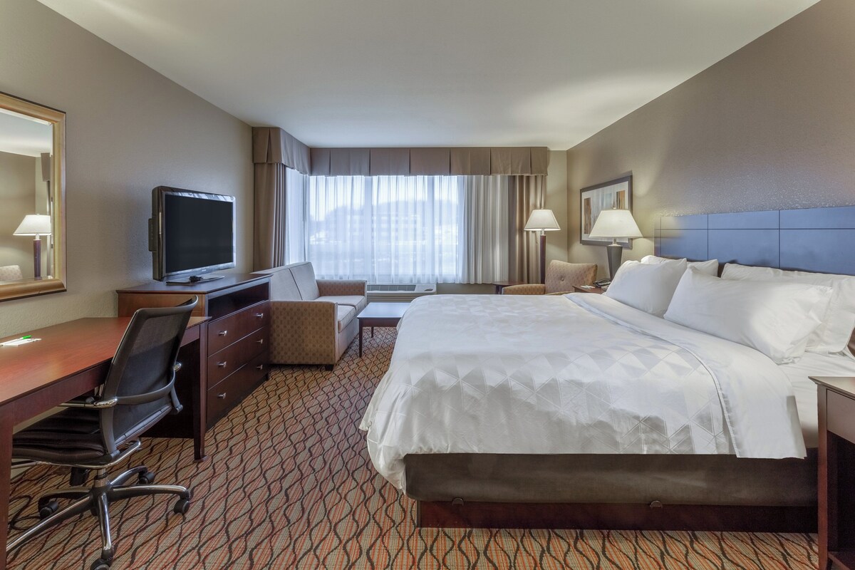 Habitación de hotel con cama, escritorio, silla, televisión y ventana con cortinas.