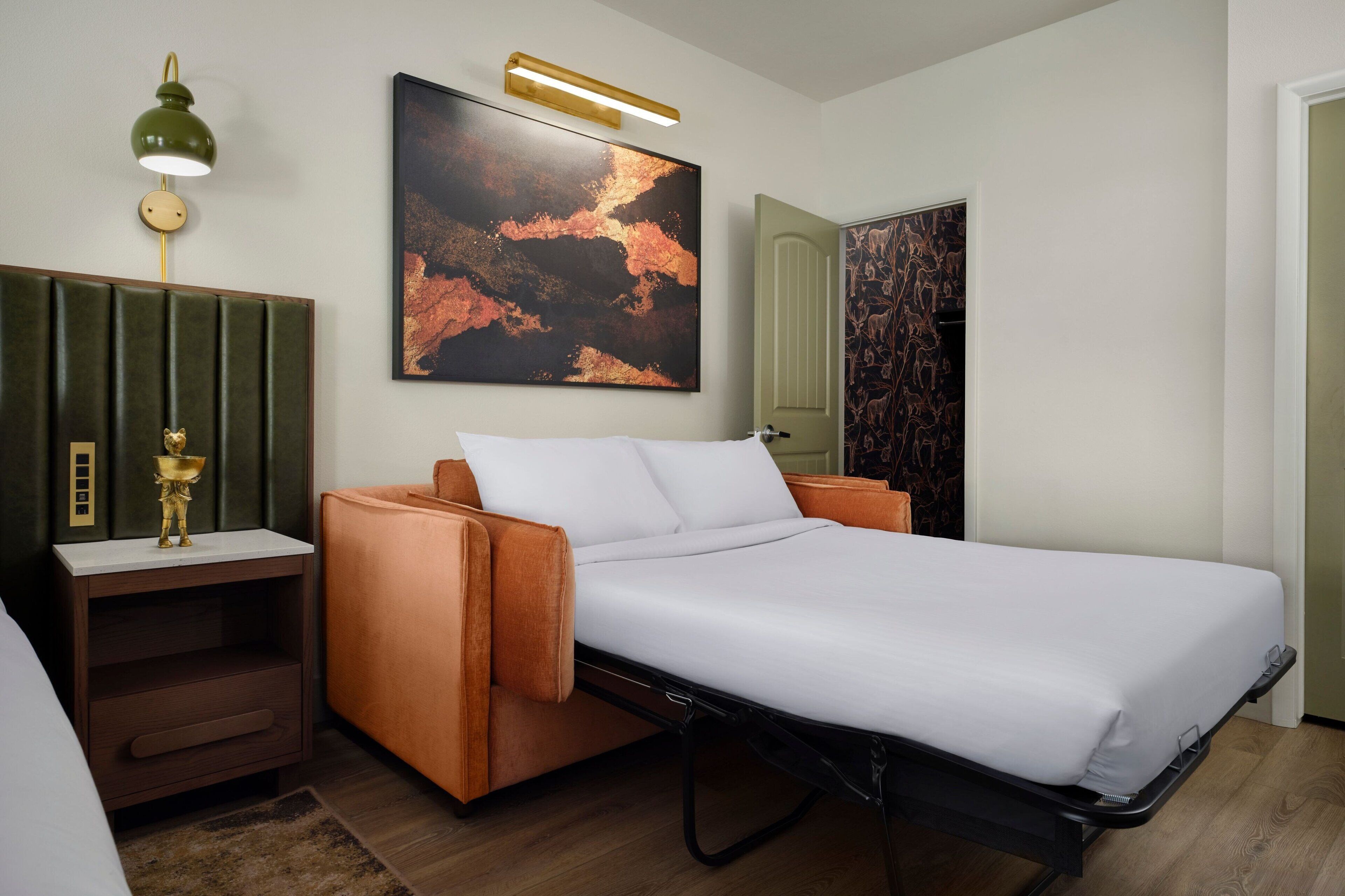 Een moderne slaapkamer met een bed, nachtkastje, lamp en een groot abstract schilderij aan de muur.