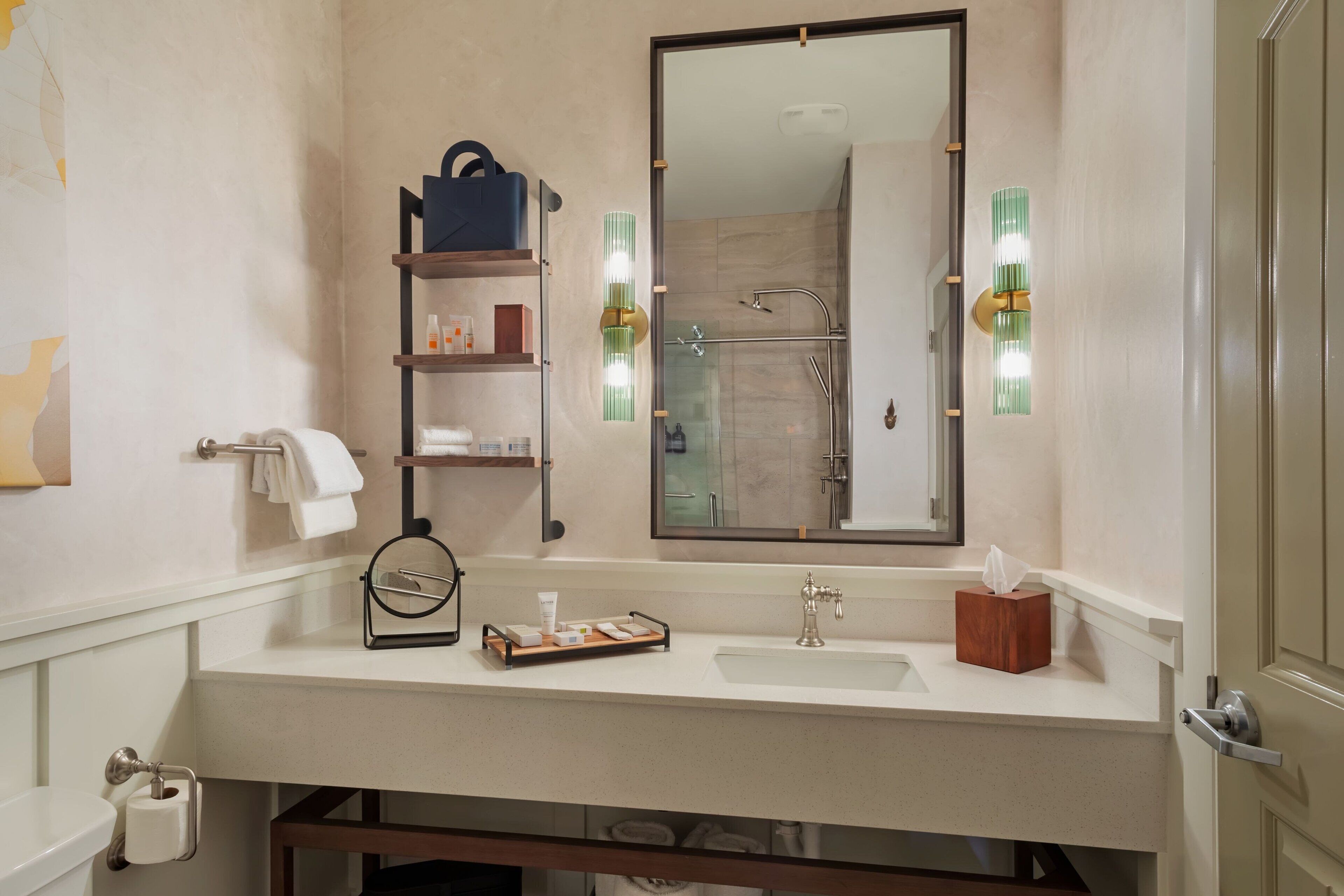 A modern bathroom with a large mirror, a sink, a towel rack, and a shelf with toiletries.