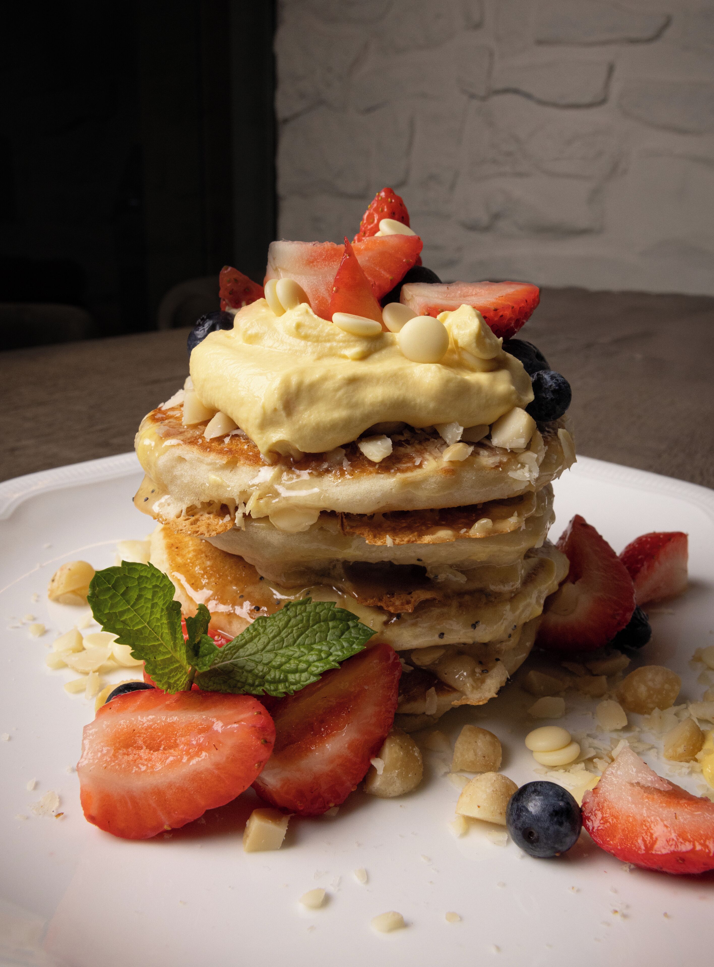 A stack of pancakes with fruit and whipped cream on a plate.