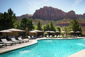 A swimming pool with lounge chairs and umbrellas, surrounded by trees and mountains.