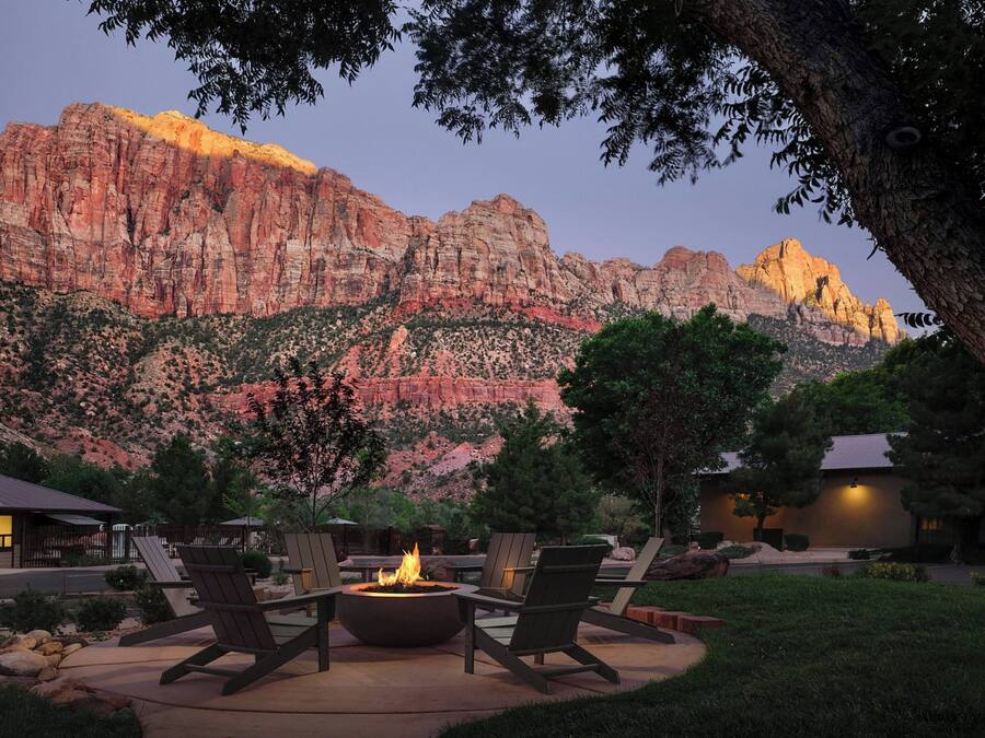 An outdoor seating area with a fire pit, surrounded by chairs, set against a backdrop of red rock formations and a mountain.