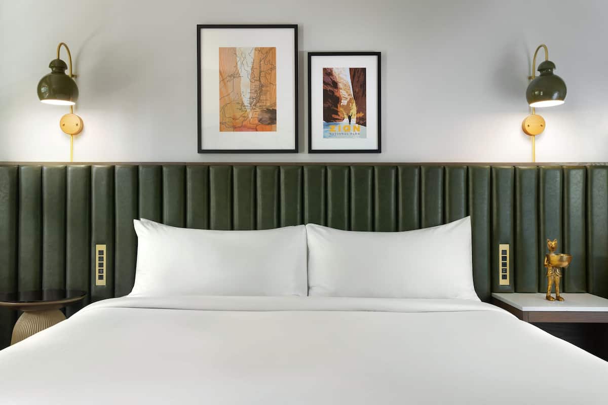 A hotel room with a large bed, two framed pictures on the wall, and two bedside lamps.