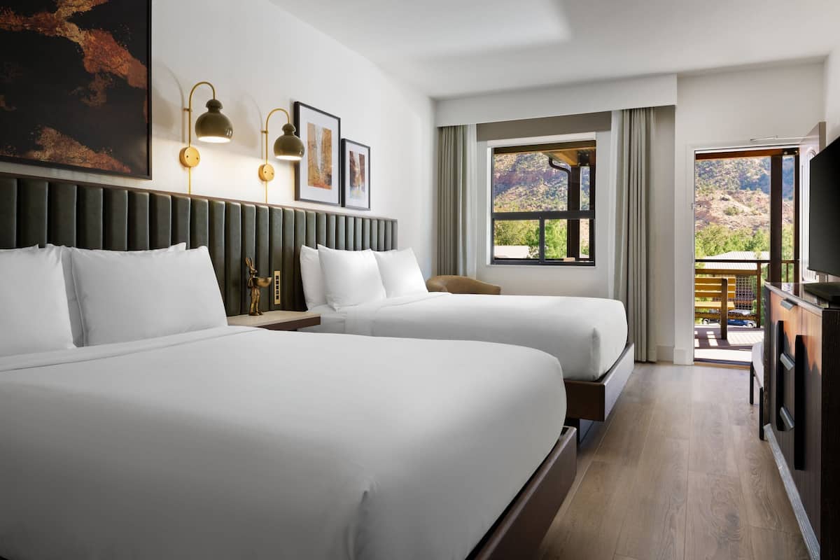 A hotel room with two beds, a large window with a view, a television, and a small table.