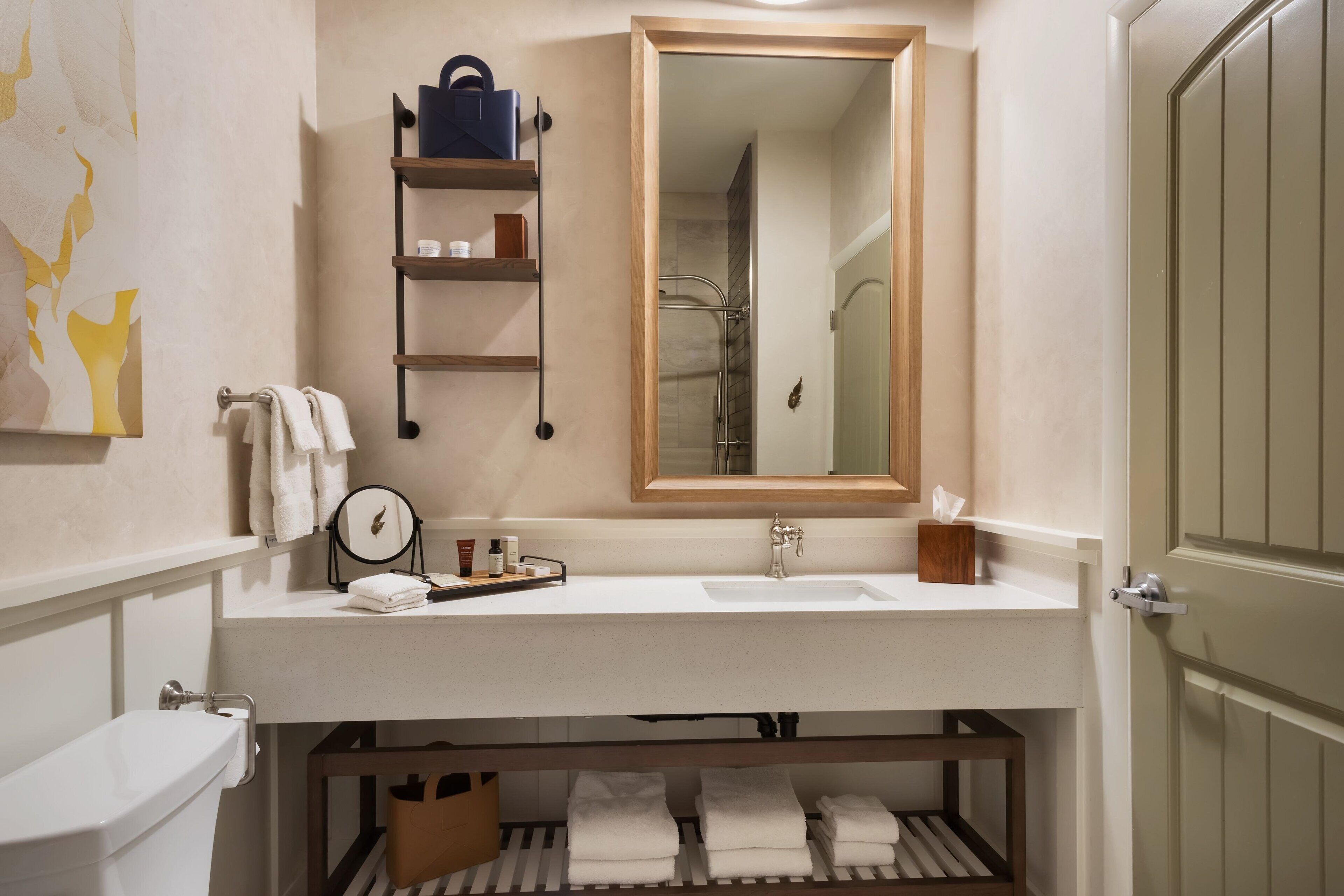 Un baño con lavamanos blanco, espejo, toallero y repisa con artículos de aseo.