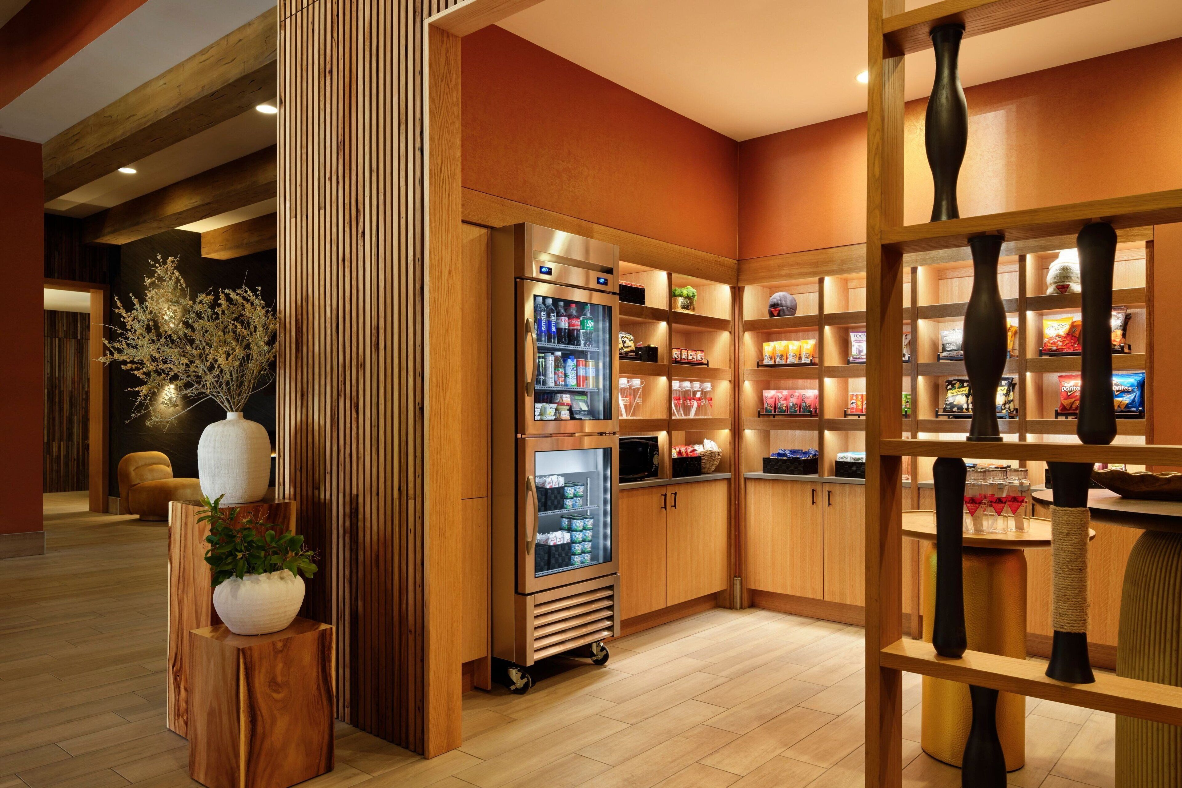 En moderne hotellobby med en træreception, en køledisk og et udvalg af snacks samt drikkevarer.