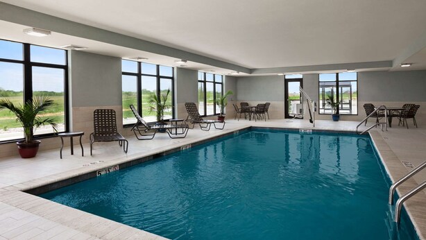 An indoor swimming pool with clear views through large windows, surrounded by lounge chairs and tables.