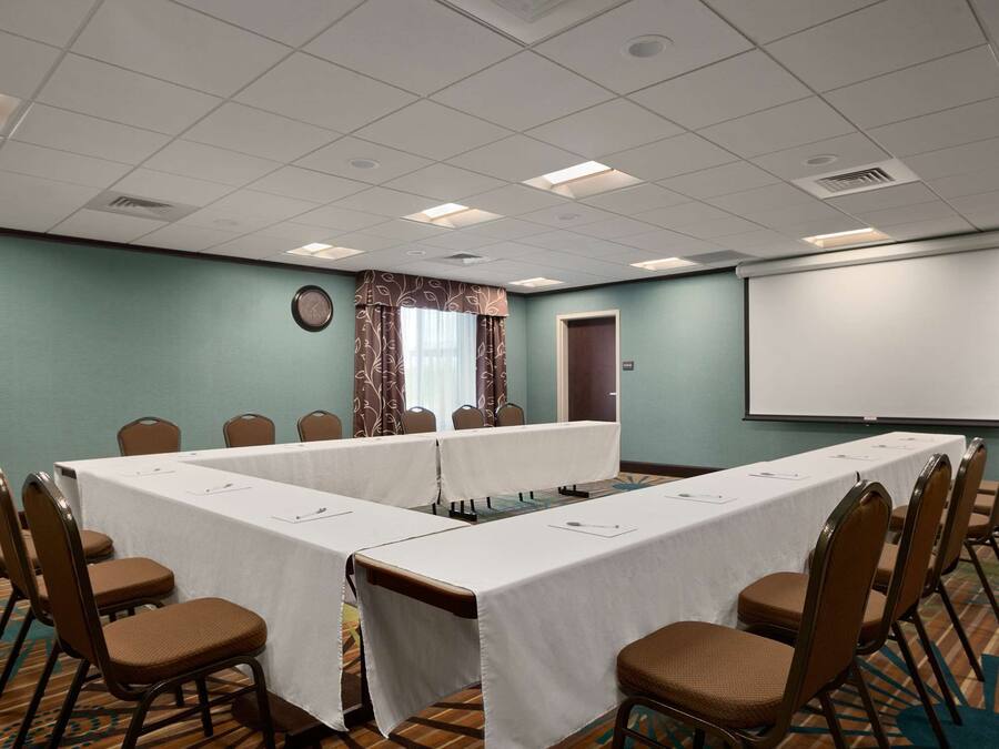 A conference room with a long table, chairs, a projector screen, and a clock on the wall.