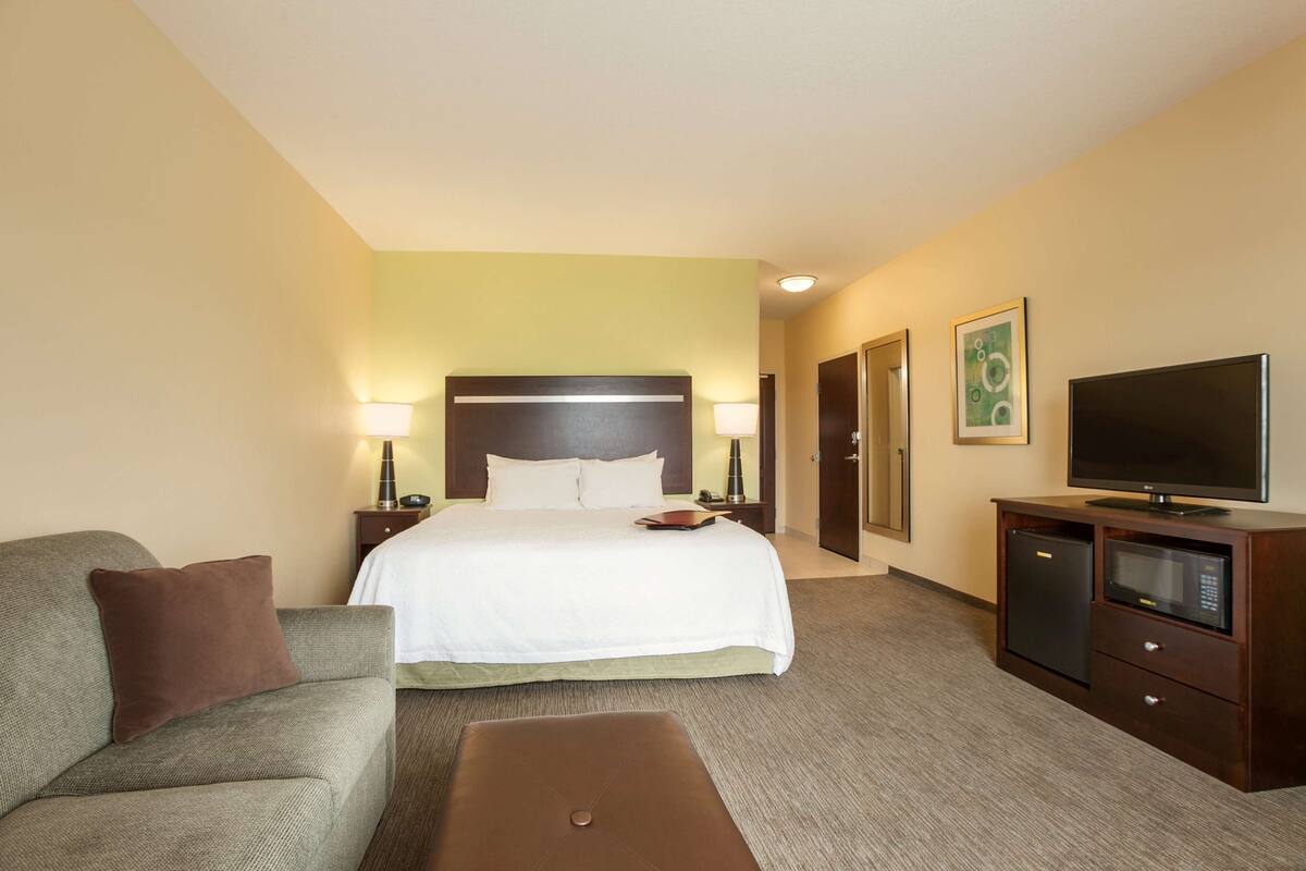 A hotel room with a bed, a sofa, a TV, a desk with a computer, and a door.