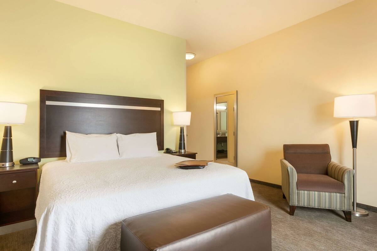 A hotel room with a bed, bedside tables, a chair, a lamp, and a mirror.