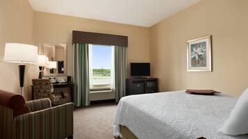 Une chambre d’hôtel avec un lit, un bureau avec une lampe, une chaise, une télévision et une fenêtre avec des rideaux.