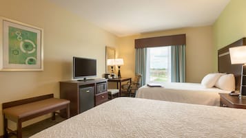 A hotel room with two beds, a desk with a TV, a chair, a bench, and a window with curtains.