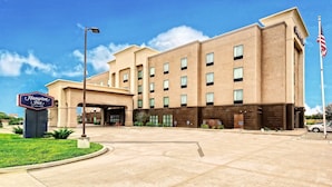A Hampton Inn by Hilton building with a clear sky, a parking lot, and an American flag.