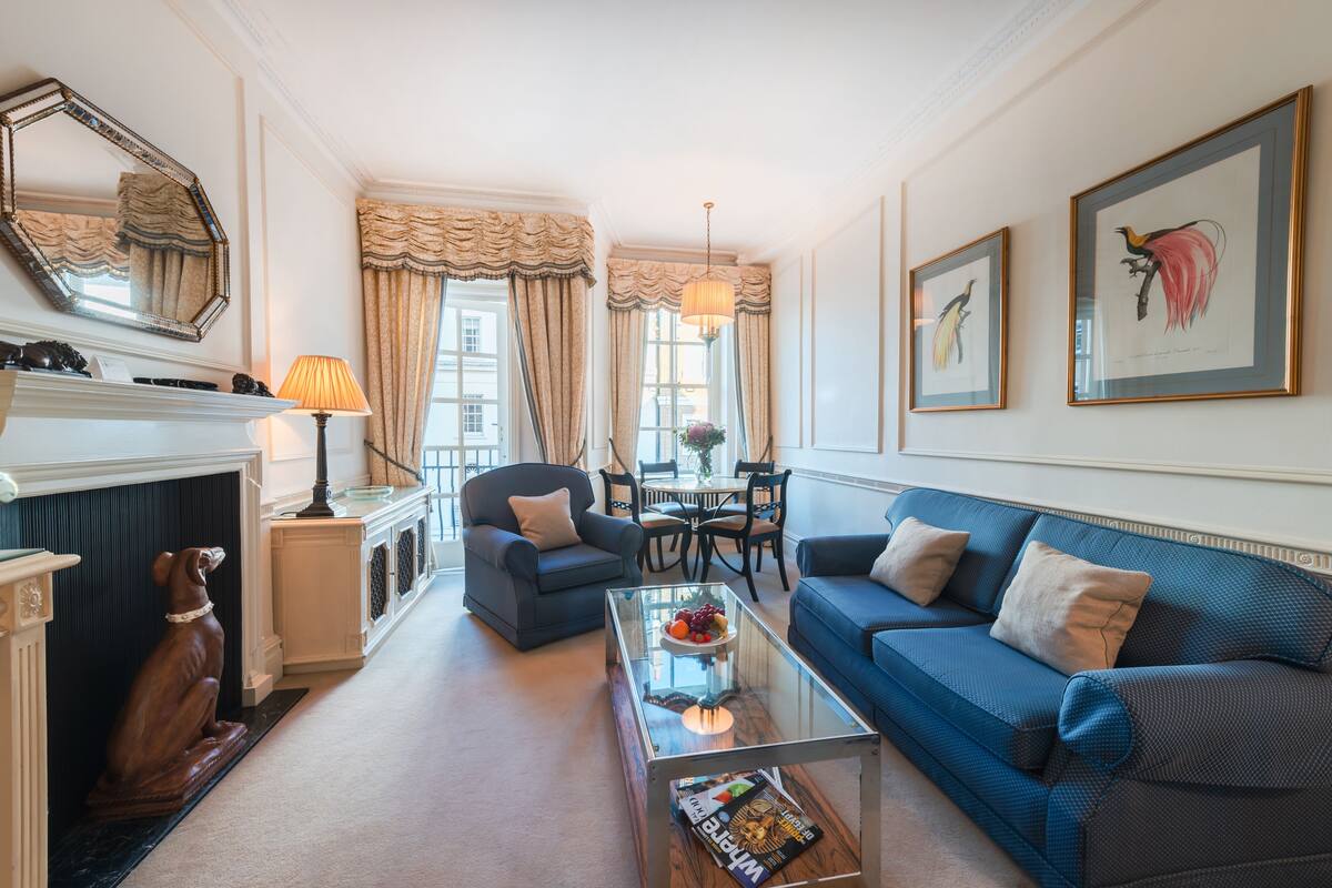Een woonkamer met een blauwe bank, een glazen salontafel, een open haard en een eethoek met een kroonluchter.