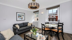 A modern living room with a grey sofa, a coffee table with a vase and newspaper, and a dining area with a round table and chairs. - Curzon Street by Mansley (London)