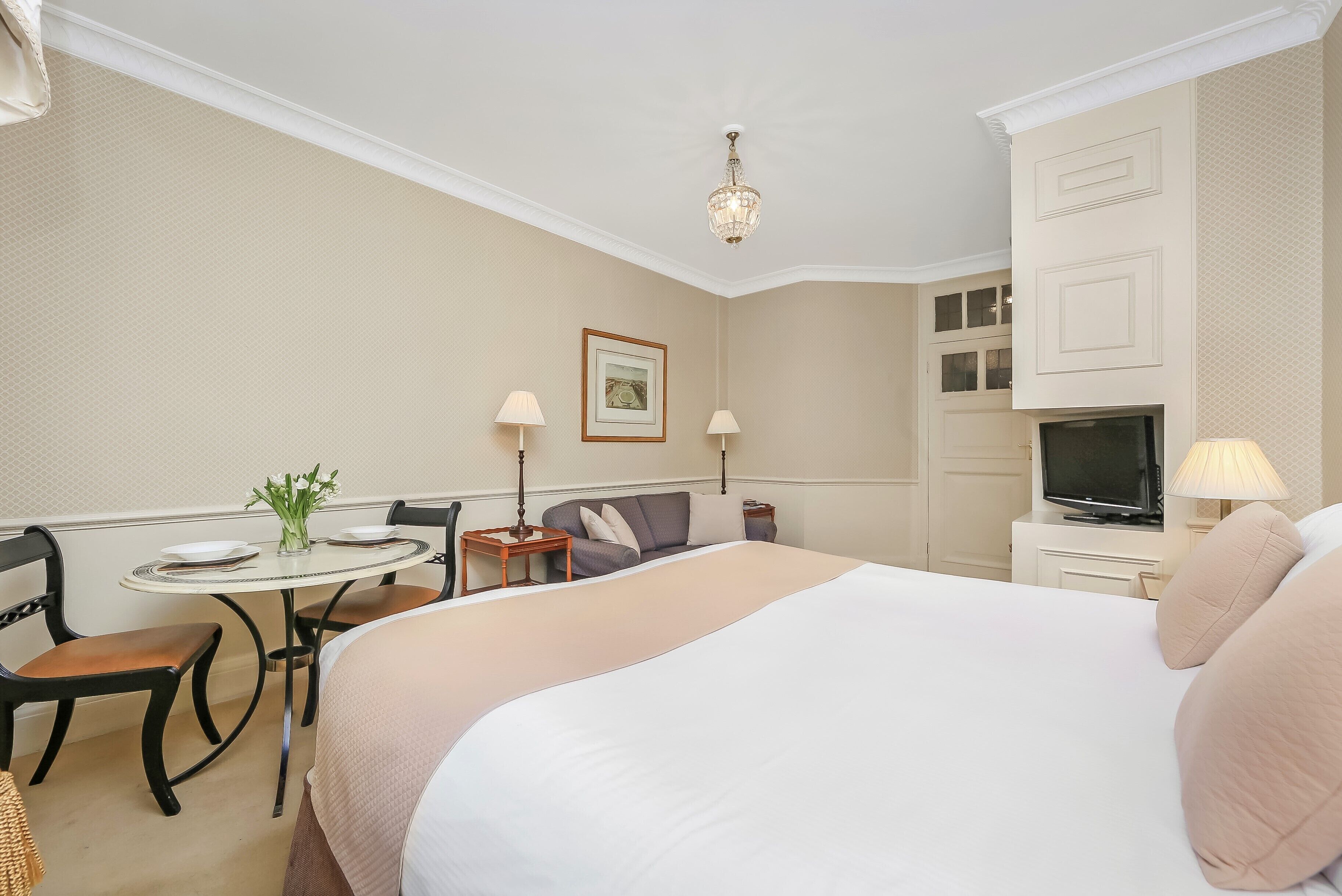 Une chambre d’hôtel avec un grand lit, un bureau avec une chaise, une télévision et une petite table sur laquelle se trouve un vase.