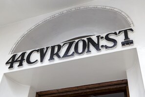 A street sign with the name "44CVRZONST" mounted on a white wall above a wooden door frame.