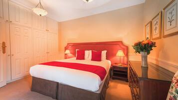 A neatly arranged bedroom with a large bed, bedside lamps, a dresser, and a vase of flowers.
