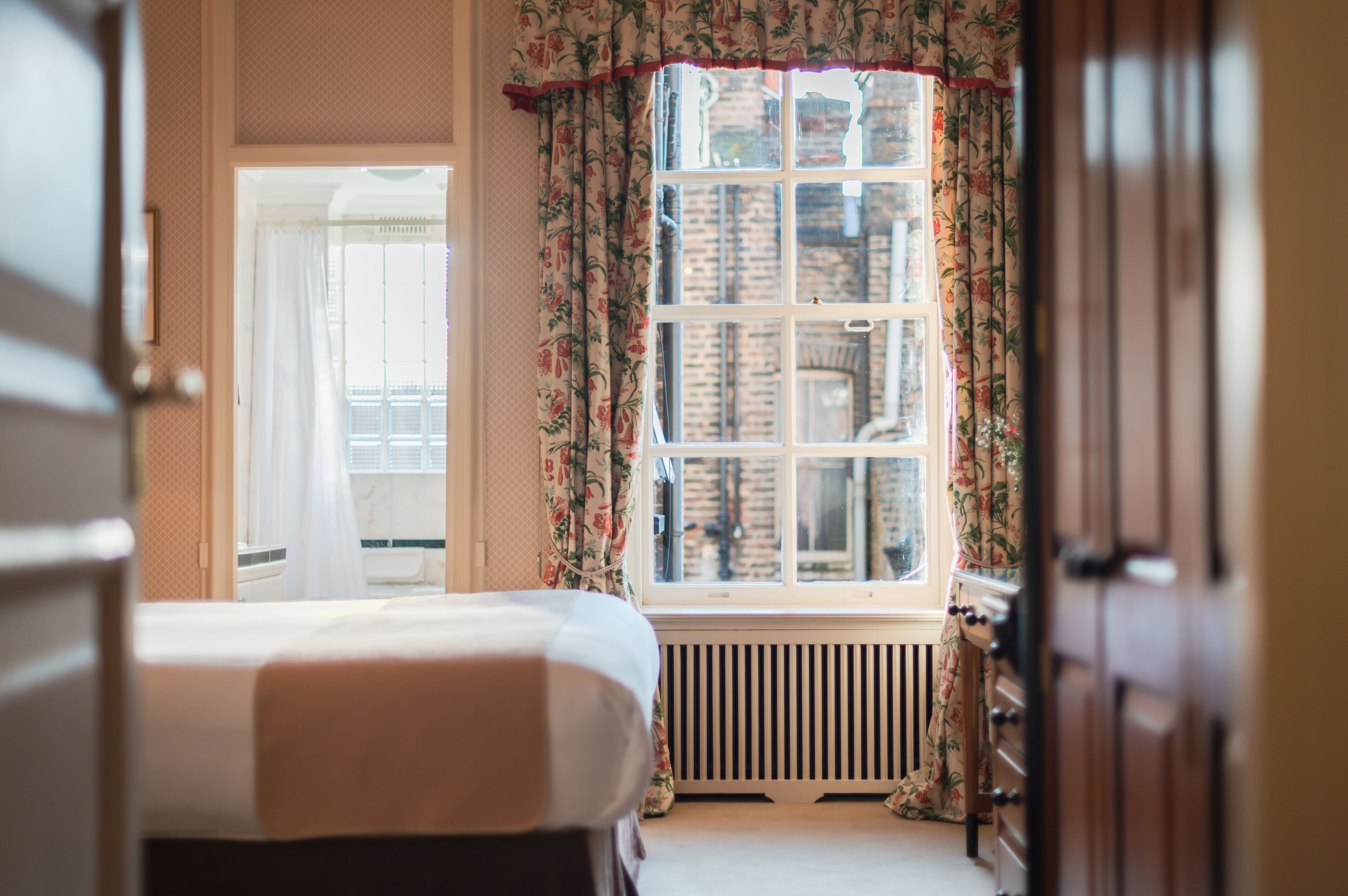 Un dormitorio con cama, radiador y ventana con cortinas florales.