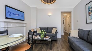 A modern living room with a dining table, a sofa, and a television displaying 'byMANSLEY'. - Curzon Street by Mansley (London)