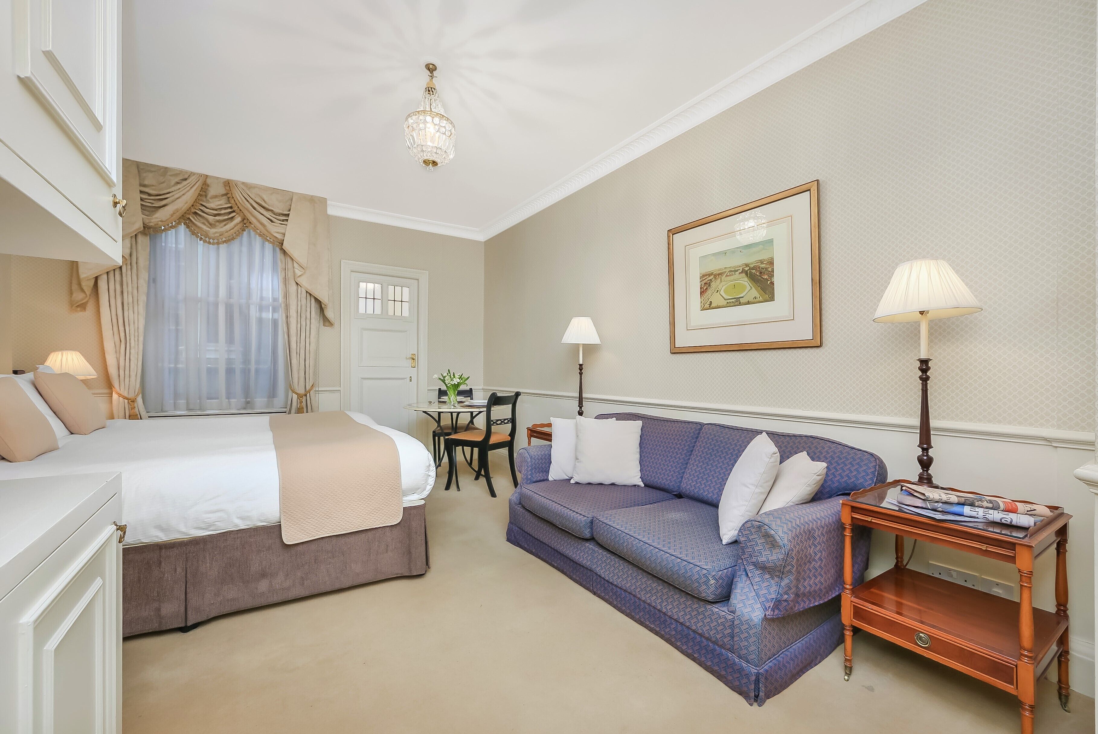 A hotel room with a bed, a sofa, a dining table with chairs, and a lamp.