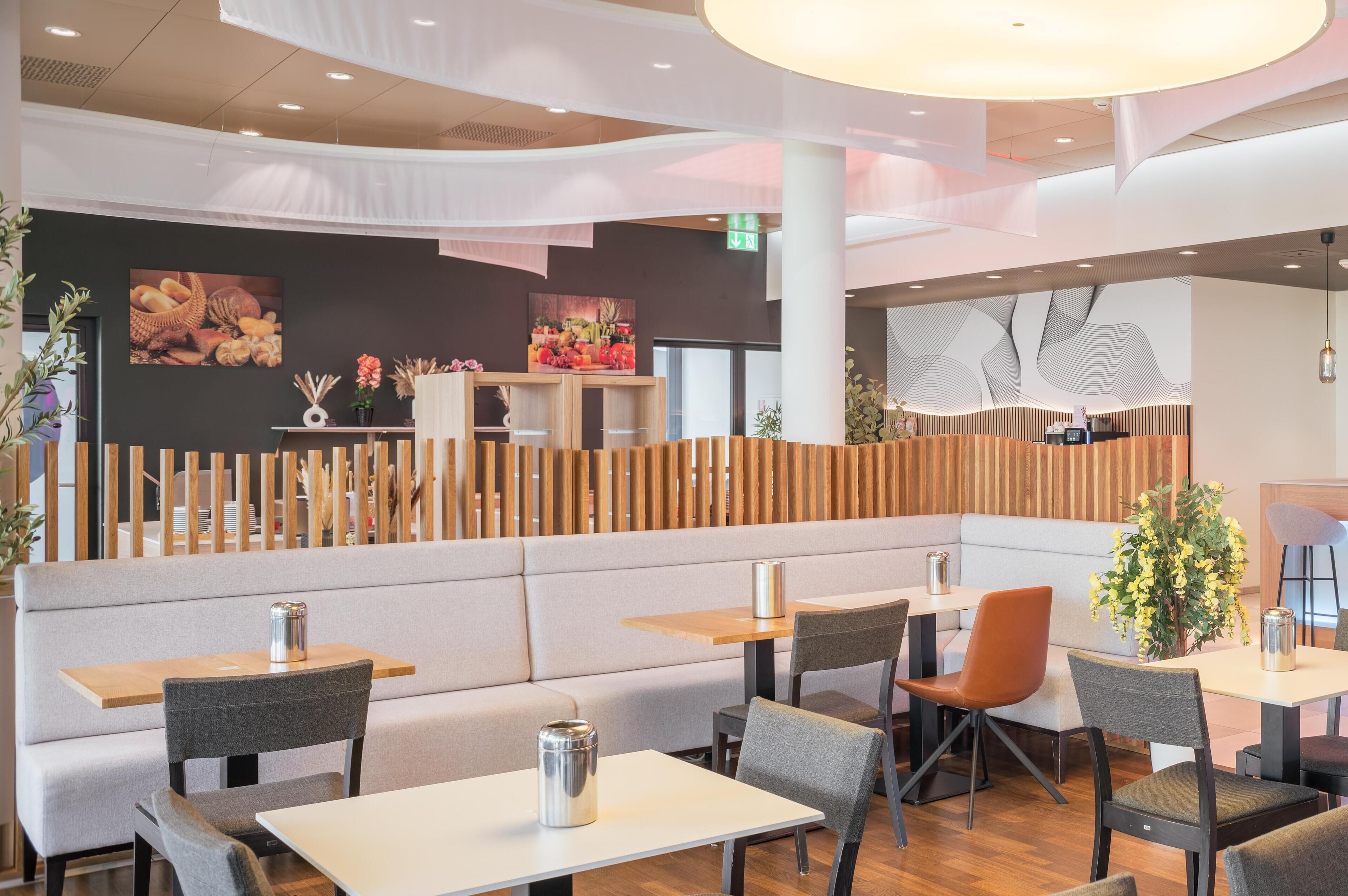 A modern restaurant with booths and tables, wooden partitions, and decorative plants.