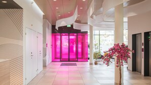 A modern hotel lobby with a bright pink elevator, a reception desk, and a potted plant. - Prize by Radisson, Zurich Affoltern am Albis (Affoltern am Albis)