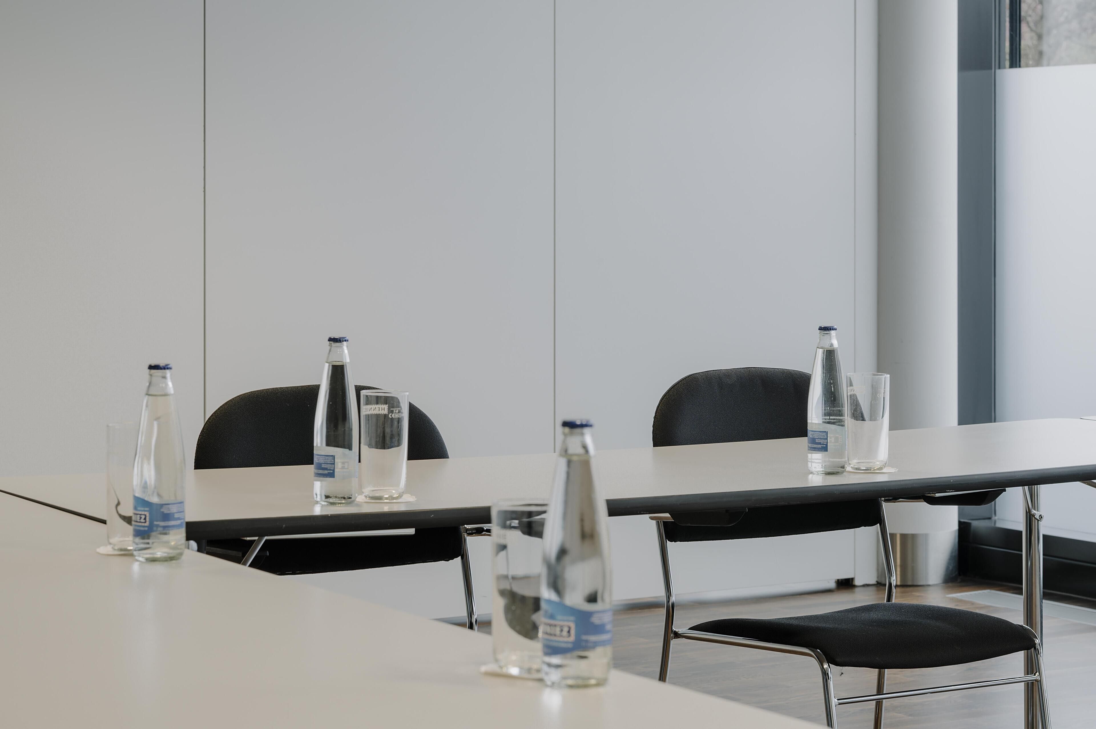 Ein Konferenzraum mit einem langen Tisch, vier Stühlen und Wasserflaschen.