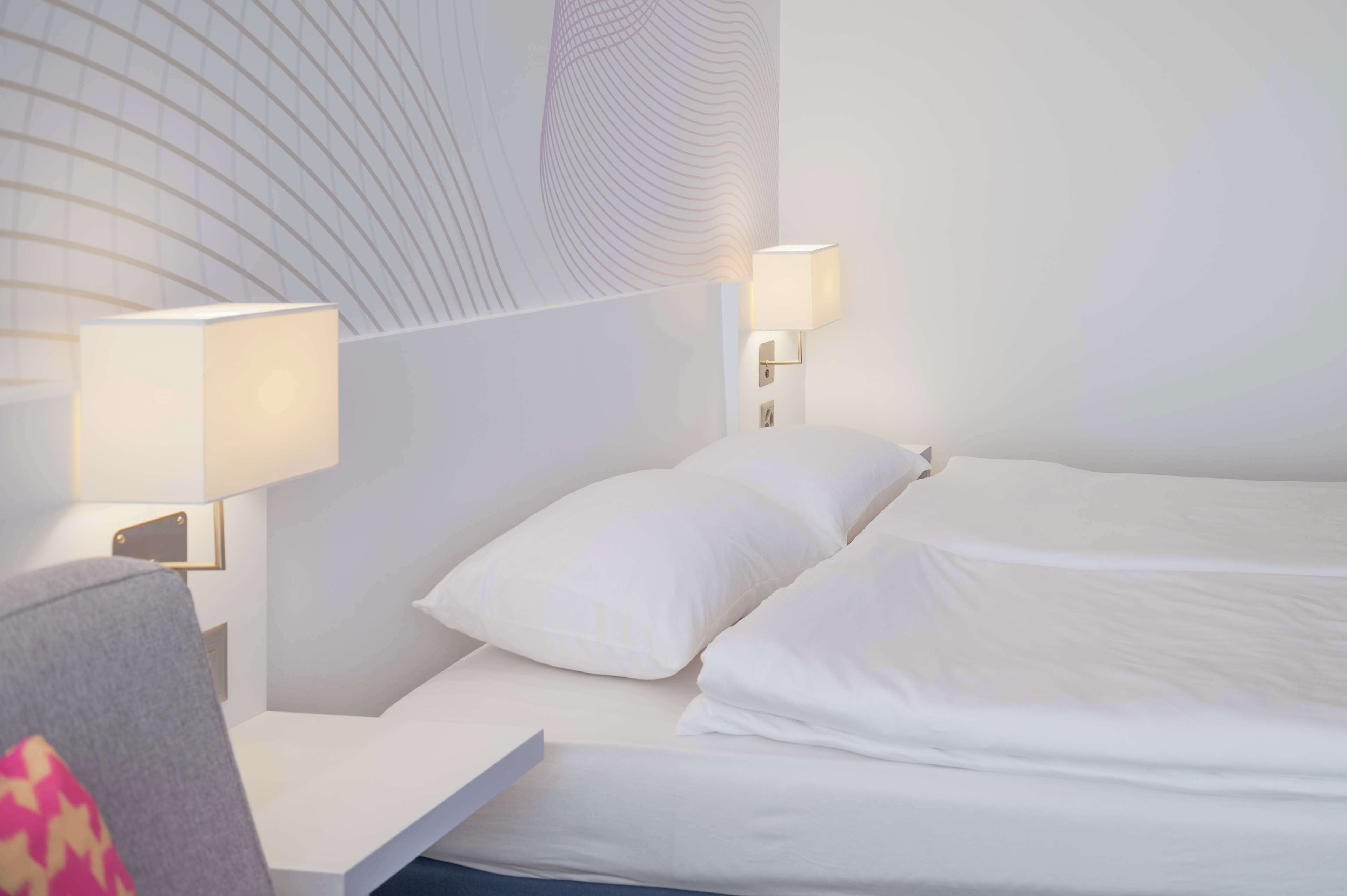 Et hotelværelse med en pænt redt seng, en sengebordlampe og en væg med et bølget mønster.