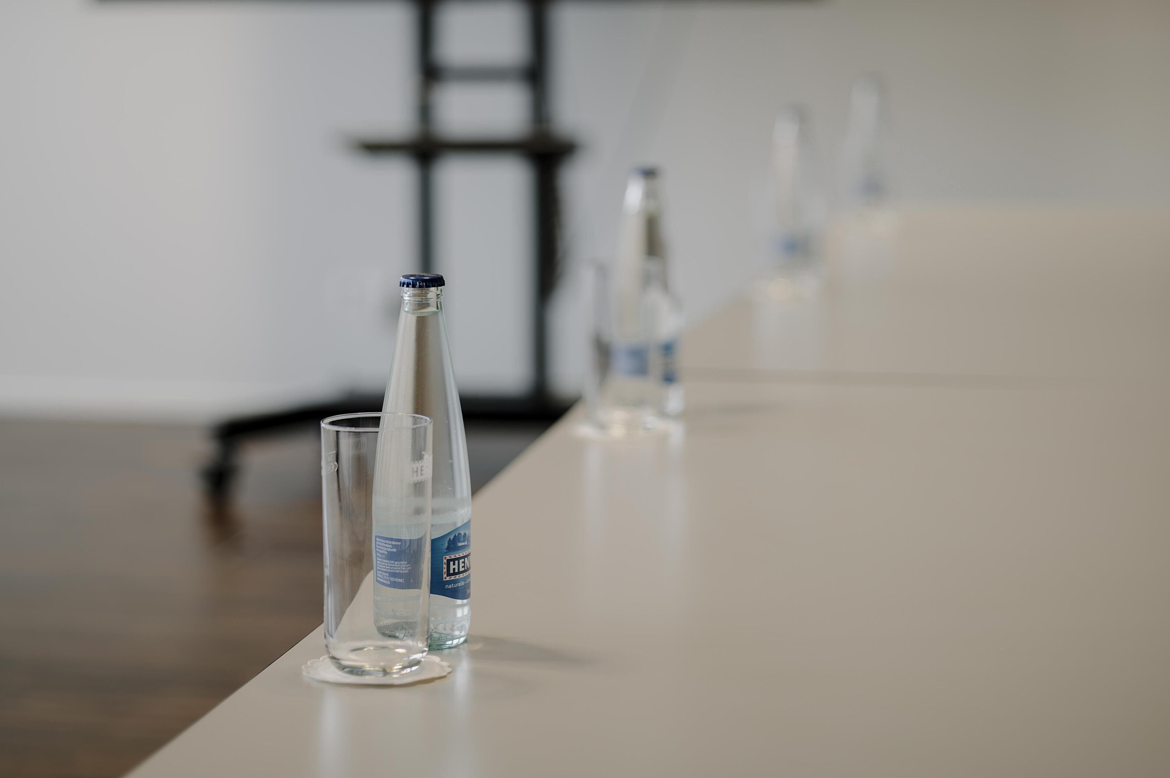 A long, narrow table with clear glass bottles and a single glass in the foreground.