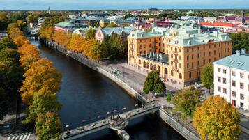 A river with a pedestrian bridge, surrounded by autumn-colored trees and historic buildings.