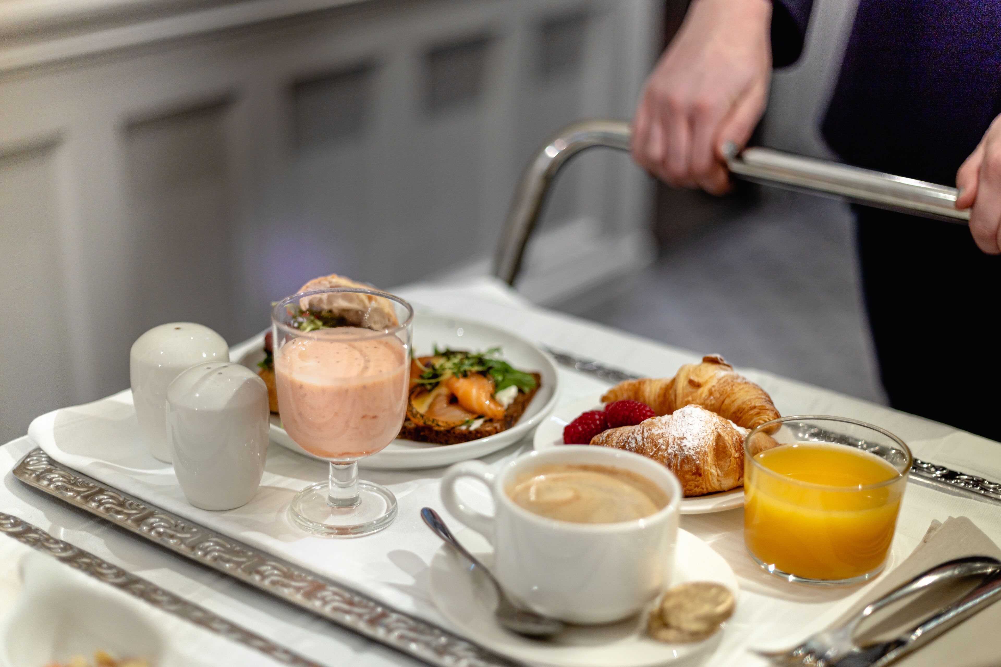 A breakfast tray with croissants, a glass of orange juice, a cup of coffee, a glass of smoothie, and a plate with a croissant and berries.