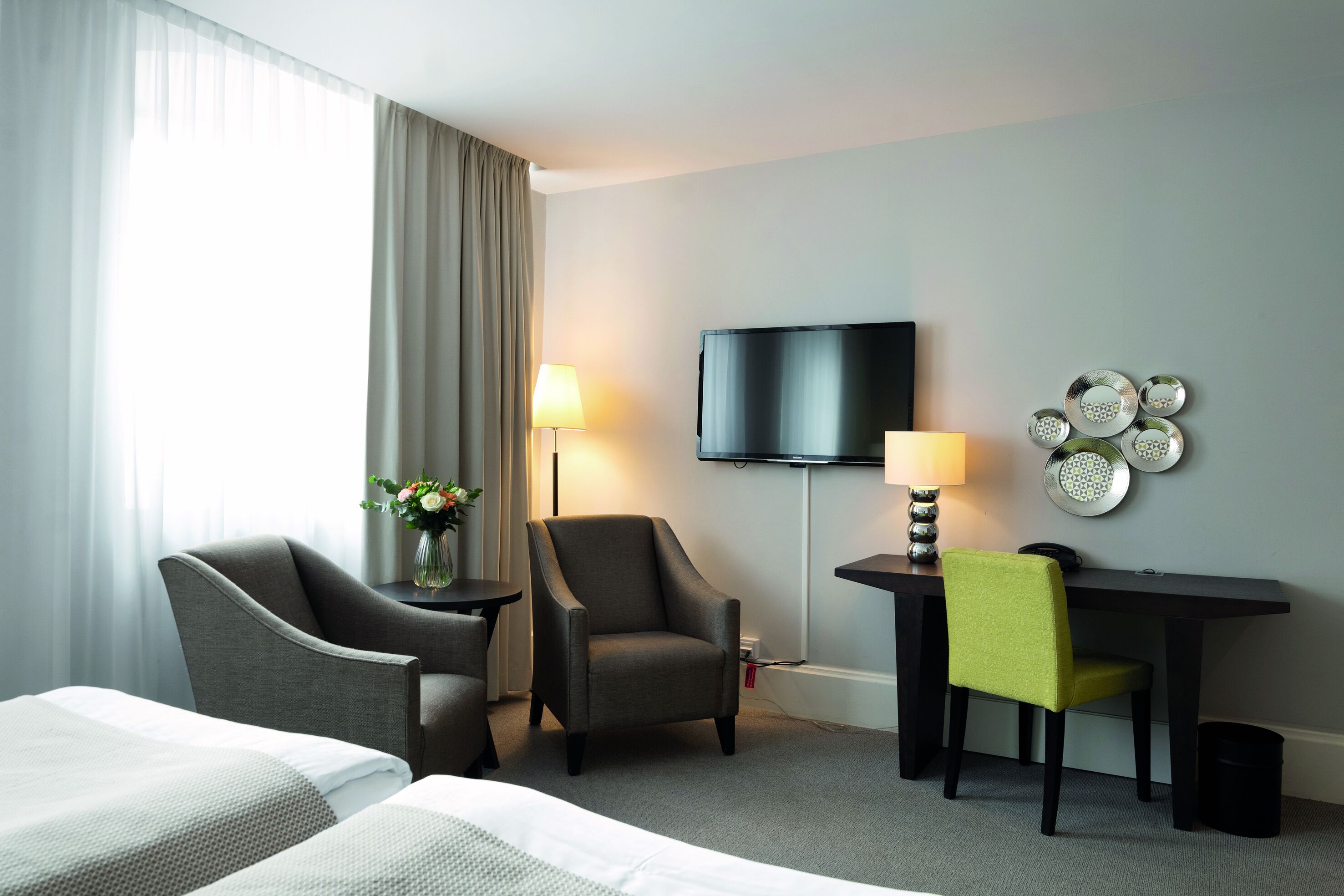 A hotel room with two single beds, a desk with a chair, a television, and a lamp.