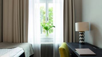 Habitación de hotel con cama, escritorio con lámpara, silla y ventana con cortinas.