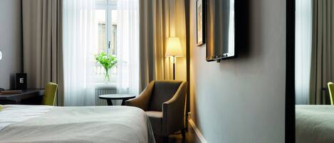 A hotel room with a bed, a chair, a desk, a lamp, and a TV.