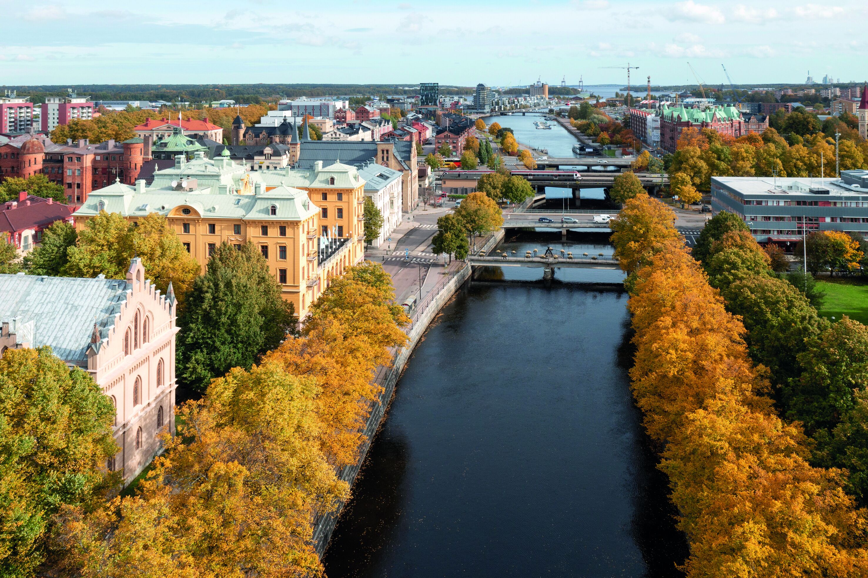 Een rivier die door een stad stroomt, met historische gebouwen en herfstkleuren.
