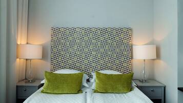 Una cama bien tendida con dos almohadas verdes, dos lámparas de noche y un cabecero estampado.