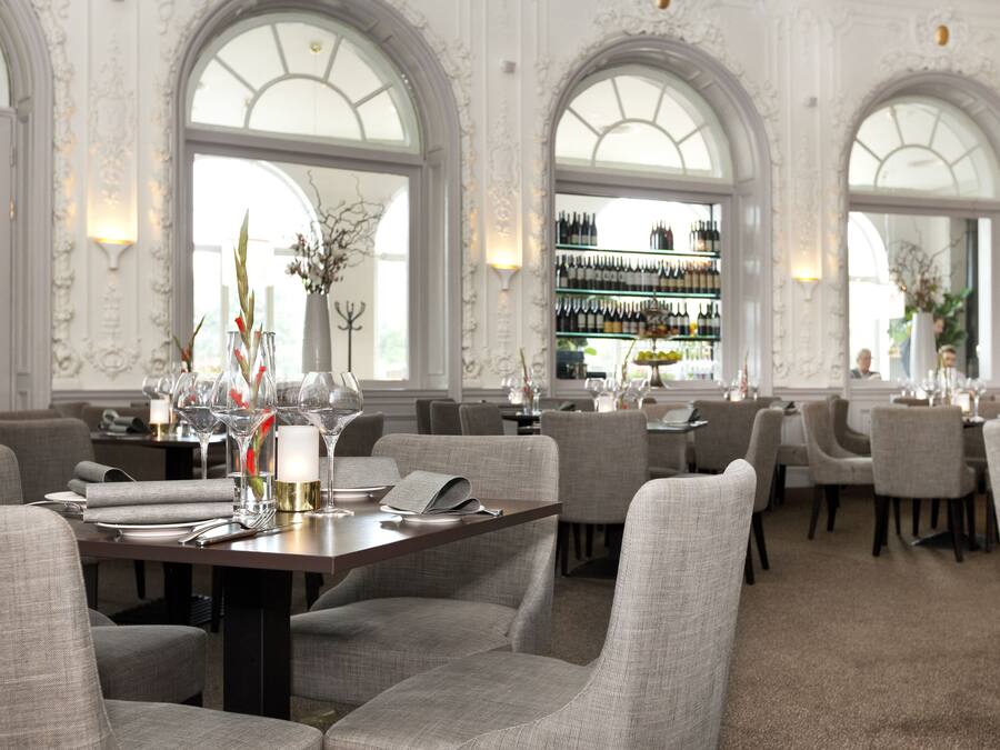 A dining area with tables set for service, upholstered chairs, and a wine display in the background.