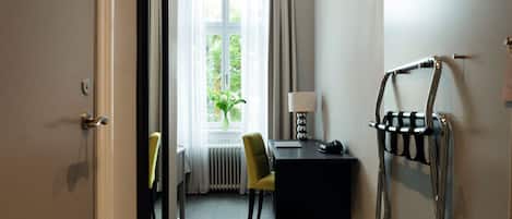 Habitación de hotel con piso de madera, un escritorio negro con lámpara, una silla y un radiador.
