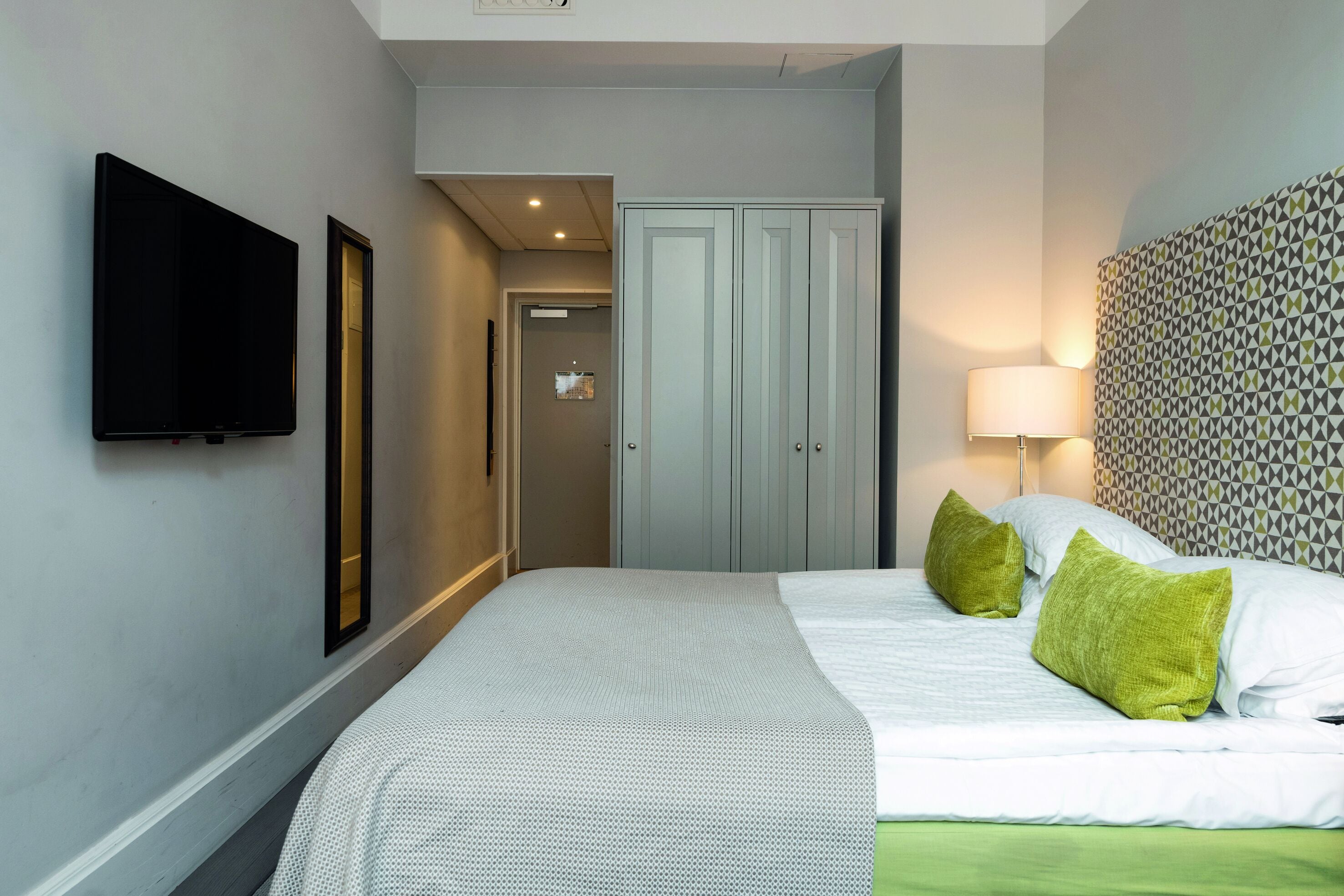 Een hotelkamer met een bed, een televisie, een kledingkast en een behang met patroon.