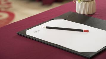 A table with a red tablecloth, a black folder, a pen, and a small potted plant.